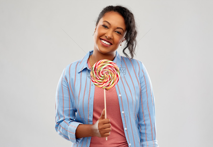 人们,糖果糖果快乐的非裔美国轻妇女与大棒棒糖粉红色背景快乐的非裔美国妇女与大棒棒糖图片