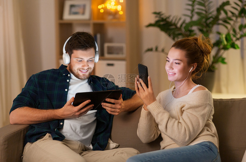 休闲,技术人的快乐的夫妇与平板电脑,耳机智能手机听音乐家里晚上家里听音乐的图片