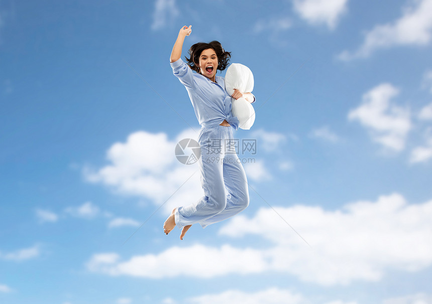 趣,人们睡前的快乐的轻女人充满活力的蓝色睡衣抱着枕头,跳过蓝天云彩的背景帕贾马的快乐女人用枕头跳过天空图片