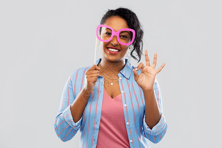 好丽友派派道具,照片亭人的快乐的非裔美国轻妇女戴着大眼镜,灰色背景上OK手标志带着大眼镜的快乐非裔美国女人背景