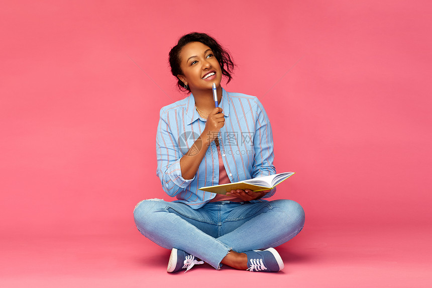 教育,高中灵感快乐的非裔美国轻学生妇女,笔日记笔记本坐地板上,思考粉红色的背景日记笔记本思维的学生女人图片
