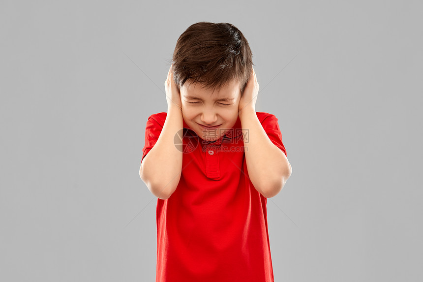 噪音,压力人的压力大的小男孩红色马球T恤耳朵手灰色背景穿红色的男孩穿着红色T恤,双手合耳图片