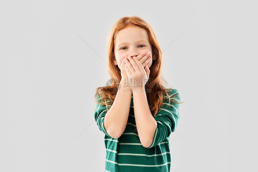 童,尴尬情感的困惑的红头发女孩穿着绿色条纹衬衫,用手遮住她的嘴灰色的背景上困惑的红头发女孩用手捂住嘴图片