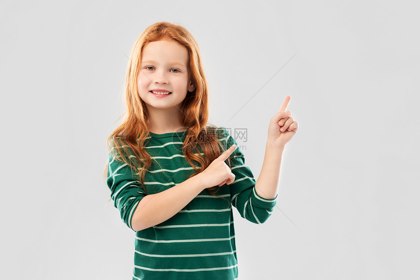 童,时尚人的微笑的红色头发女孩穿着绿色条纹衬衫,指着灰色背景上的东西微笑的红头发女孩手指向上图片