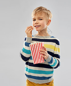 小男孩抬着水桶快餐,垃圾食品童的小男孩穿条纹套头衫吃爆米花纸桶灰色背景小男孩纸桶里吃爆米花背景