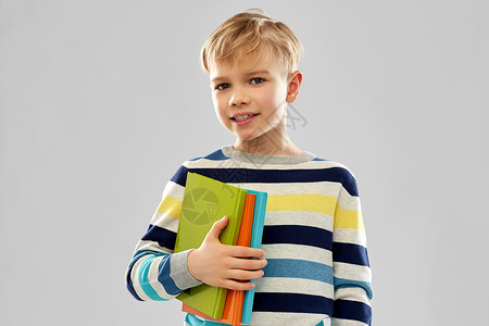 条纹毛衣学校,教育人的小学生男孩的肖像与书籍灰色背景带书的小学生男孩背景