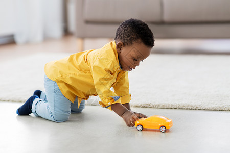 蹒跚学步的孩子童,孩子人的可爱的非裔美国男孩玩黄色玩具汽车地板上家里非裔美国小男孩玩玩具车背景