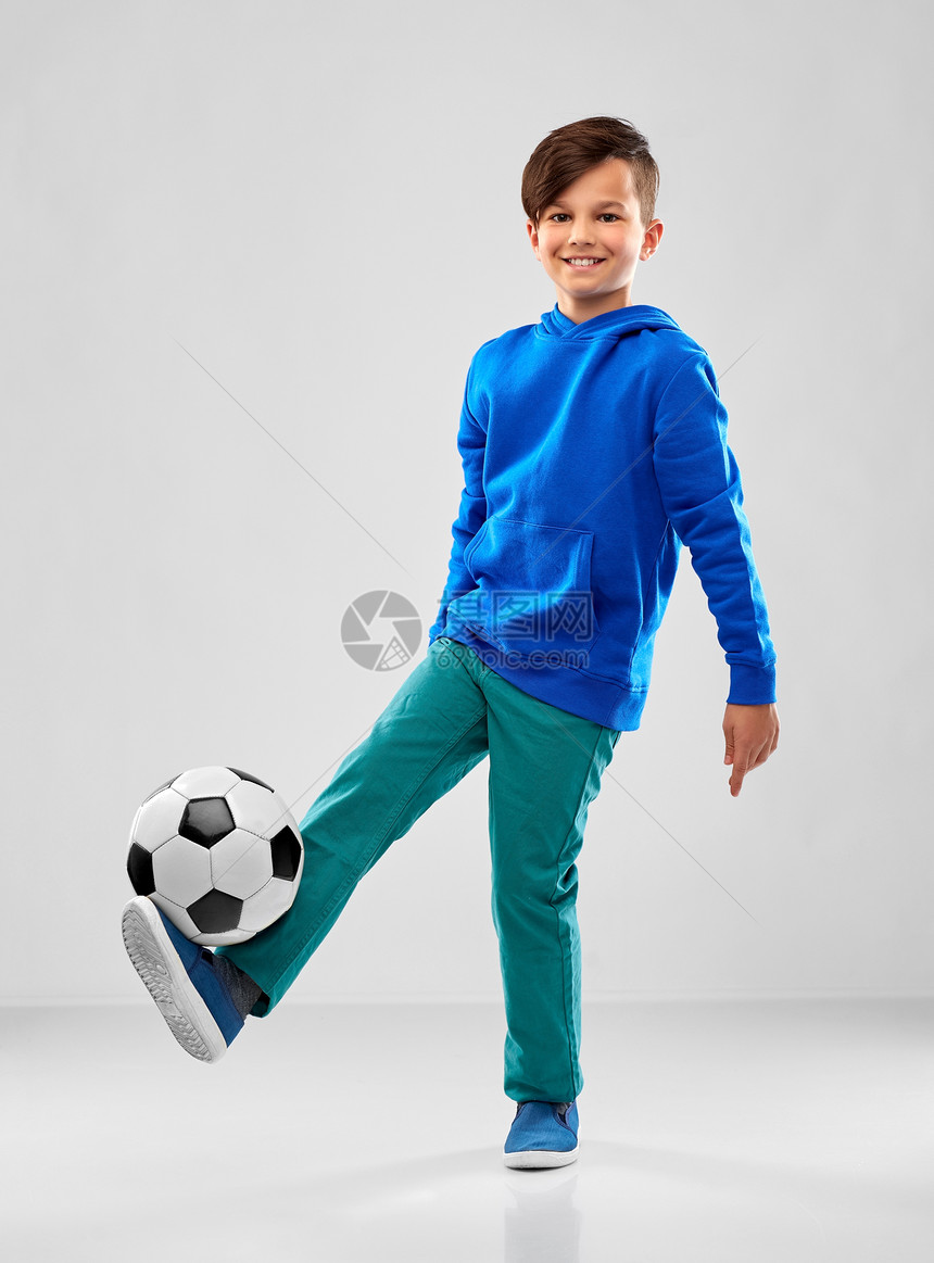 童,足球体育微笑的男孩穿着蓝色帽衫灰色背景下踢足球穿着蓝色帽衫的微笑男孩踢足球图片