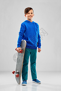 童,休闲人的微笑的男孩,蓝色帽衫与滑板灰色背景带滑板的蓝色帽衫微笑的男孩图片