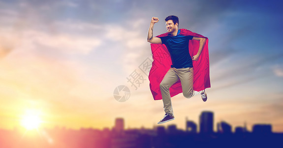 超级能量团超级力量人的快乐的轻人红色超级英雄斗篷日落上空飞行塔林背景城市穿超级英雄斗篷的人城市日落上空飞行背景