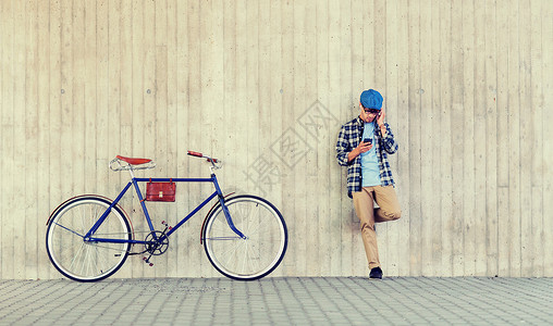 蜗耳墙人,风格,技术,休闲生活方式轻的时髦男子戴着耳机,智能手机固定齿轮自行车城市街道墙上听音乐戴着智能手机自行车的耳背景