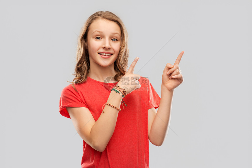 人们的微笑的十几岁女孩,长发穿着红色T恤,手指指向灰色背景上的东西微笑的十几岁的女孩指着什么图片