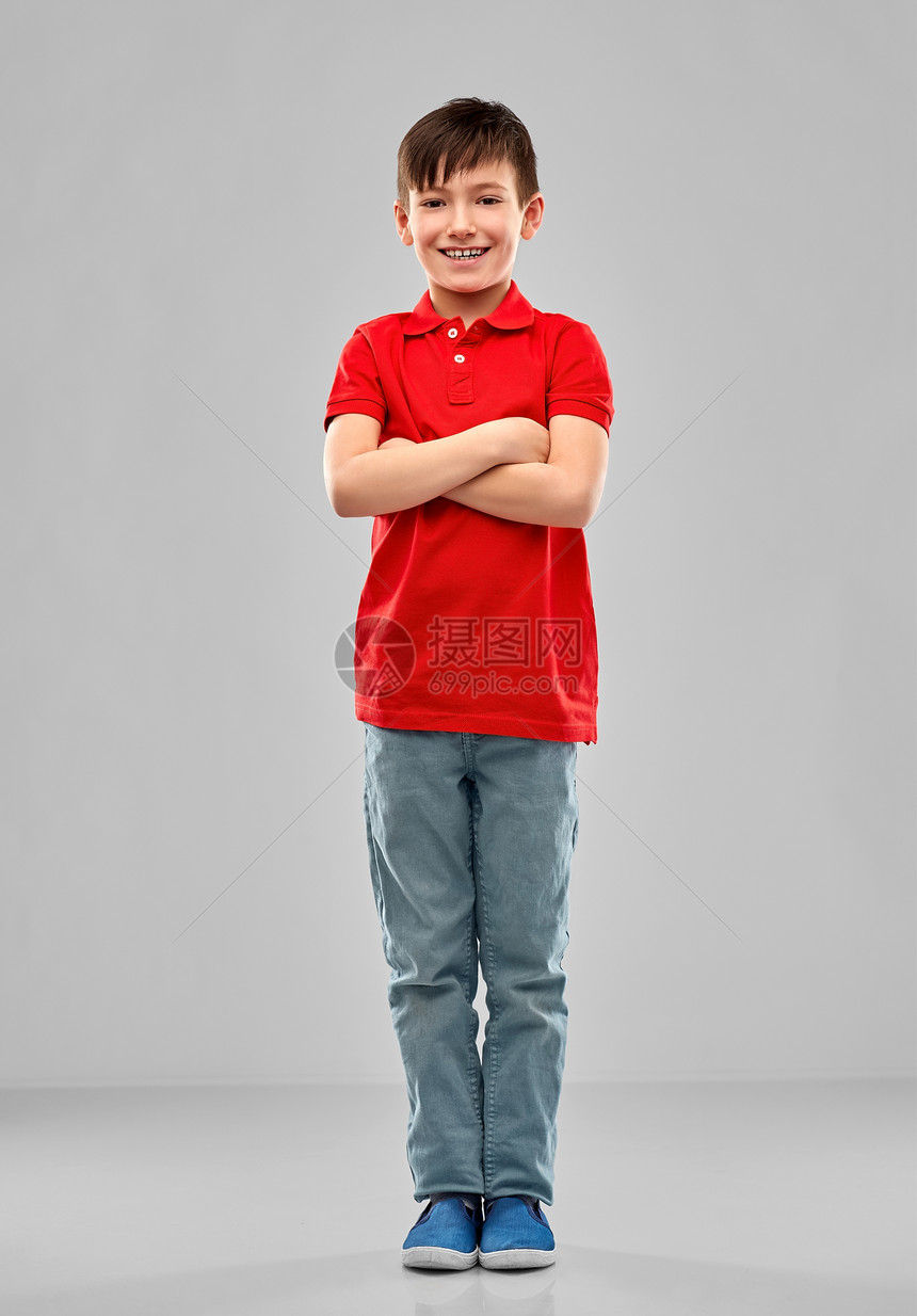 童,表情人的微笑的小男孩穿着红色马球T恤,交叉手臂灰色背景上微笑的男孩穿着红色马球T恤,双臂交叉图片