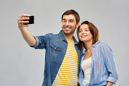 技术人的快乐的夫妇拥抱自拍智能手机灰色背景幸福的夫妇用智能手机自拍图片