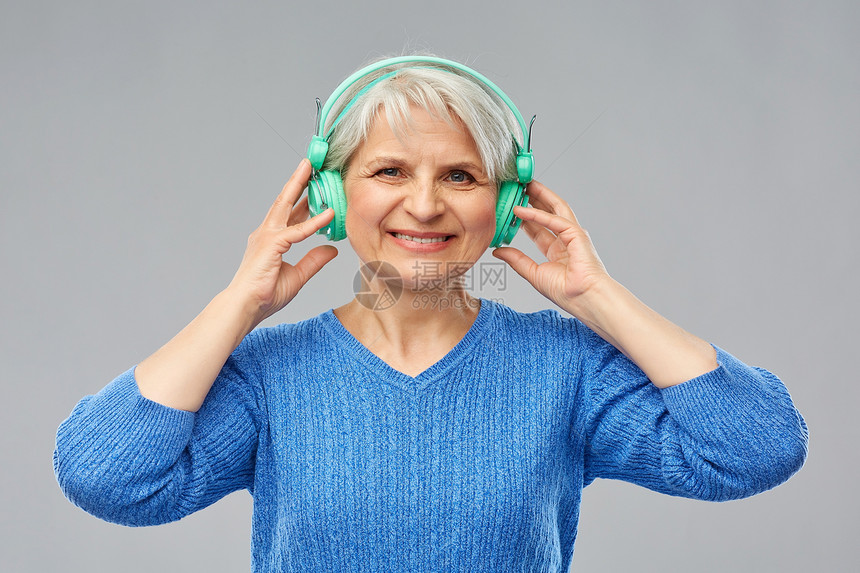 技术老人的微笑的老妇女戴着眼镜耳机,灰色背景下听音乐戴耳机听音乐的高级女人图片