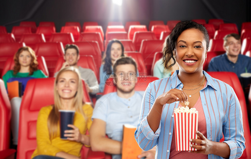 电影,快餐娱乐活动快乐的非裔美国轻妇女吃爆米花条纹桶超过人们电影院背景非洲女人电影院吃爆米花图片