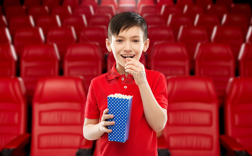 电影,快餐娱乐活动微笑的小男孩穿红色马球T恤吃爆米花蓝色纸桶电影院背景微笑的男孩电影院吃爆米花图片