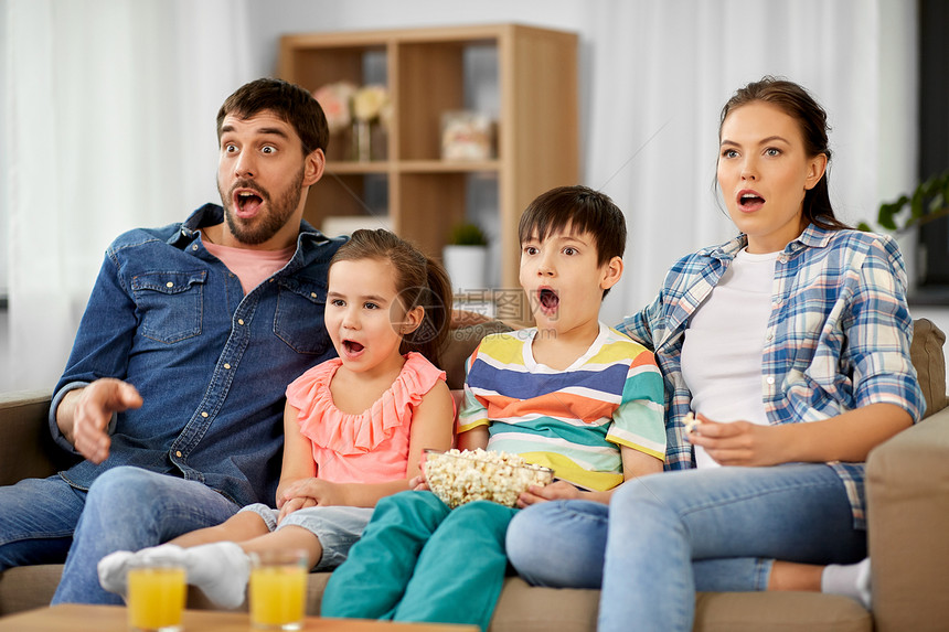 家庭休闲人的害怕惊讶的母亲,父亲,儿子女儿家里看电视上的爆米花害怕的家人带着爆米花电视上看片图片