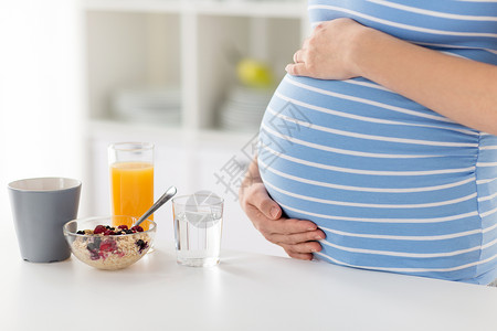 孕妇早餐怀孕,健康饮食产妇密切孕妇与早餐厨房桌子上触摸她的肚子家里靠近孕妇抚摸她的腹部背景
