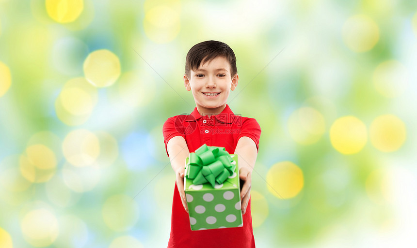 生日,童人的微笑的小男孩穿着红色马球T恤,礼品盒绿色节日灯的背景带生日礼物盒的红色T恤微笑的男孩图片
