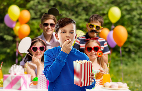快餐,童人的男孩穿蓝色帽衫,吃爆米花条纹纸桶超过群朋友生日聚会夏季公园背景男孩生日聚会上吃爆米花背景图片