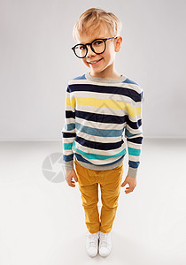 戴眼镜的小男孩学校,教育视觉微笑的小男孩穿条纹套头衫灰色背景的眼镜的肖像戴眼镜条纹套衫的微笑男孩背景