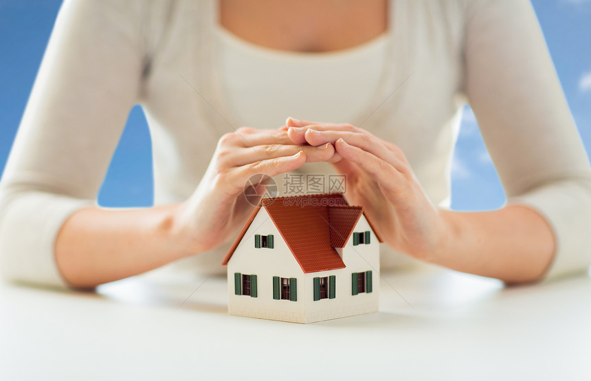 安全家庭保险的近距离的妇女保护房子的模式,手蓝天云的背景用手保护房子模型的女人图片