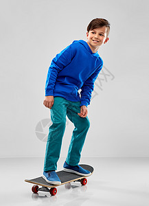 童,休闲人的微笑的男孩,蓝色帽衫与滑板灰色背景带滑板的蓝色帽衫微笑的男孩图片