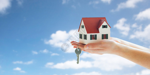 抵押贷款,房地产财产近距离的手着房子模型家庭钥匙蓝天云彩的背景双手紧握房屋模型钥匙背景图片