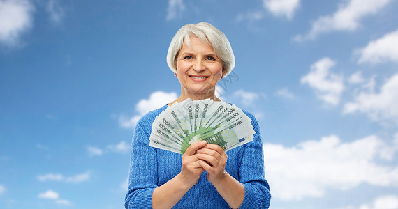 蓝色天空下的微笑的老年女子拿着钞票图片