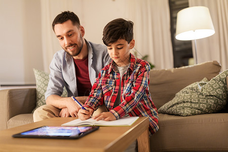 教育,家庭家庭作业的快乐的父亲儿子家里用平板电脑写笔记本父亲儿子作业图片