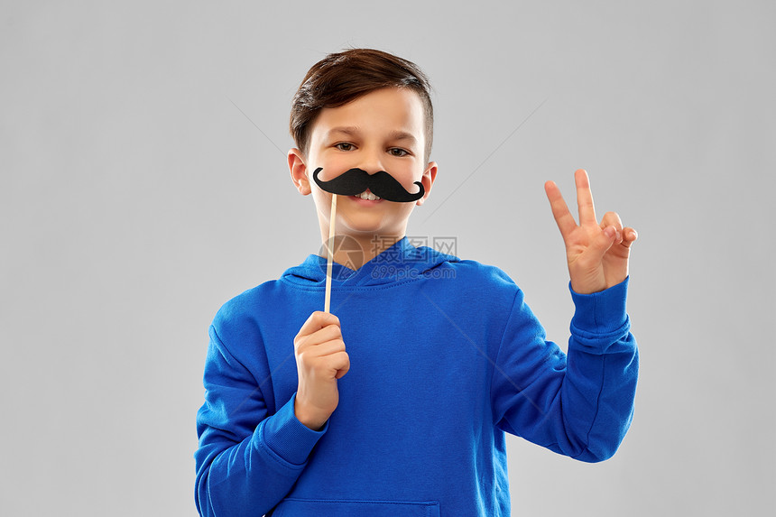 派道具,照片亭童的微笑男孩穿着蓝色帽衫,黑色胡子灰色背景上带着黑色胡子的蓝色帽衫微笑的男孩图片