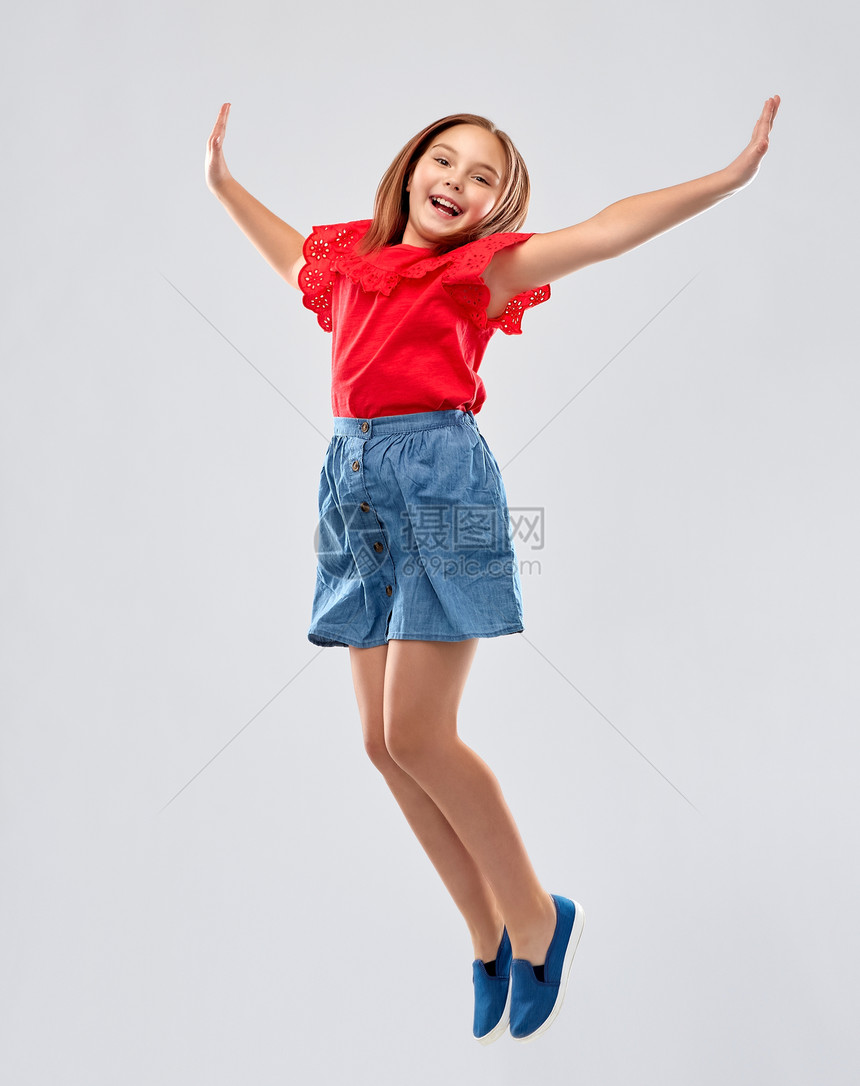 童,趣运动的快乐的微笑女孩穿着红色衬衫裙子跳过灰色的背景快乐的微笑女孩穿着红色衬衫裙子跳跃图片