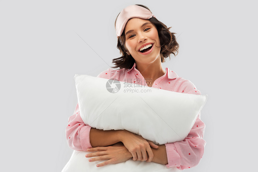 人们睡前的快乐的轻女人睡衣眼罩拥抱枕头灰色背景戴着睡衣枕头眼罩的女人图片