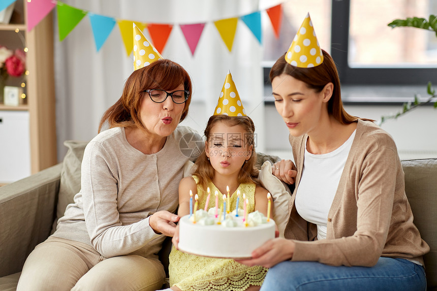 家庭,世代庆祝微笑的母亲,女儿祖母戴着派帽,家里蜡烛妈妈,女儿,奶奶带着生日蛋糕图片