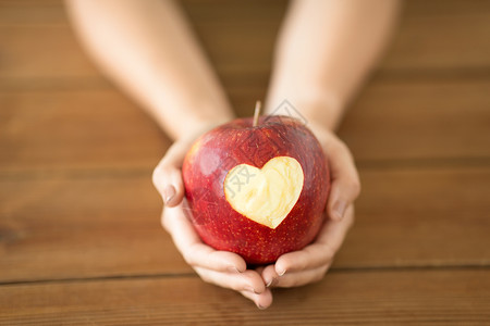 心形苹果素材食物,情人节健康密切的手,着成熟的红色苹果,雕刻的心形木制桌子上用雕刻的心紧握着苹果的手背景