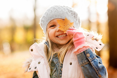 无忧无虑的少者童,季节人的快乐的小女孩与枫叶秋天的公园秋天公园里带着枫叶的快乐小女孩背景