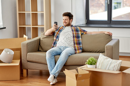 移动,人房地产的快乐的人与智能手机盒子坐沙发上的新家新家沙发上智能手机盒子的男人背景图片