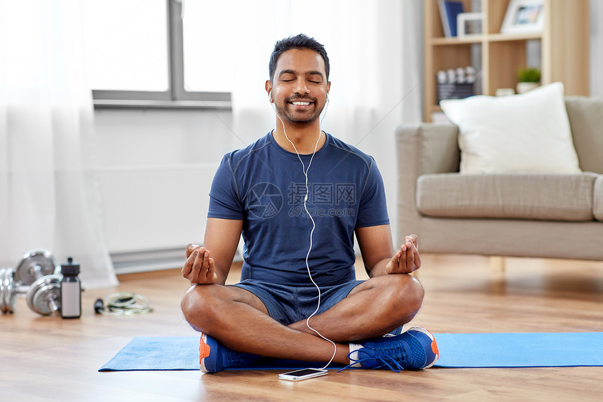 健身,冥想健康的生活方式印度男子戴着耳机,智能手机上听音乐,家里印度男人家里冥想莲花姿势图片