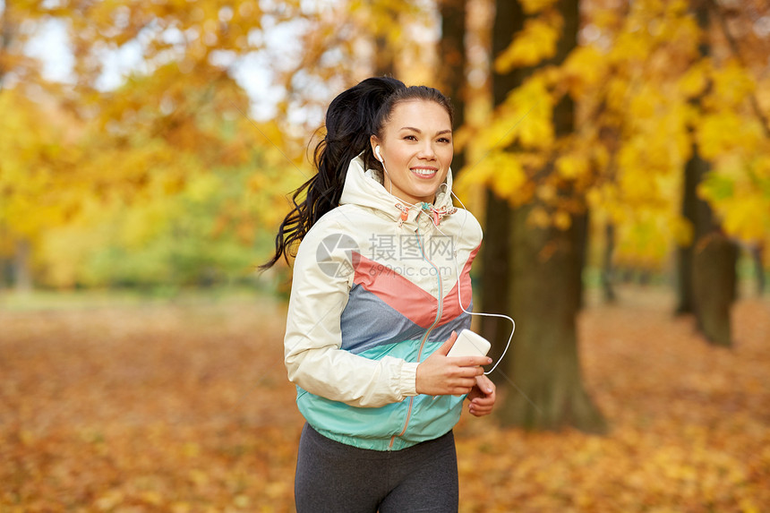 健身,运动,人健康的生活方式轻的女人带着耳机智能手机秋季公园跑步女人公园里跑步,听音乐图片