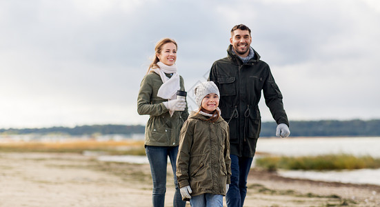家庭休闲人的快乐的母亲父亲小女儿沿着秋天的海滩散步幸福的家庭沿着秋天的海滩散步背景图片