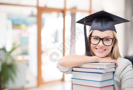 教育,毕业知识快乐的微笑研究生女孩戴着学士帽眼镜,带着学校背景的书籍研究生女孩戴着带书的学士帽背景图片