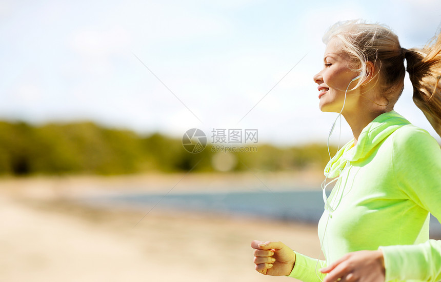 健身,运动健康的生活方式微笑的女人与耳机运行听音乐夏季海滩背景耳机的女人公园跑图片