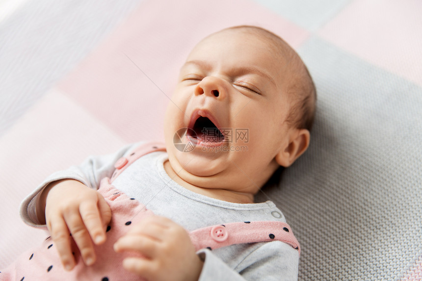 婴儿期人们的甜蜜的哈欠小女孩穿着粉红色的西装躺针毛毯上打哈欠的女婴穿着粉红色的西装躺毯子上图片