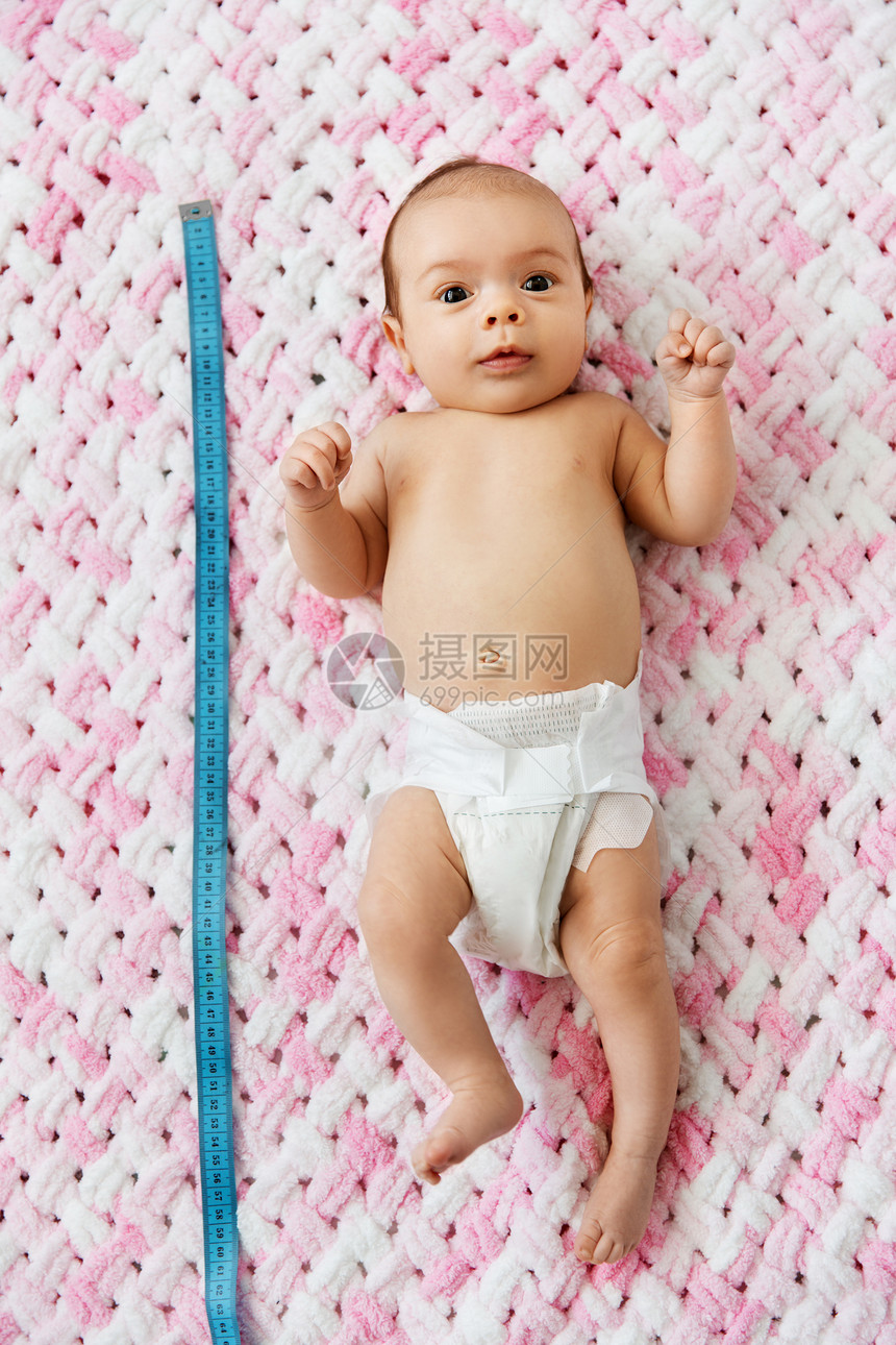 婴儿期,大小高甜蜜的小女孩尿布上躺着,用测量胶带针的粉红色毛毯毛绒纱小女孩躺毯子上用卷尺图片