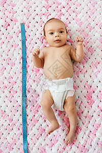 婴儿期,大小高甜蜜的小女孩尿布上躺着,用测量胶带针的粉红色毛毯毛绒纱小女孩躺毯子上用卷尺背景图片