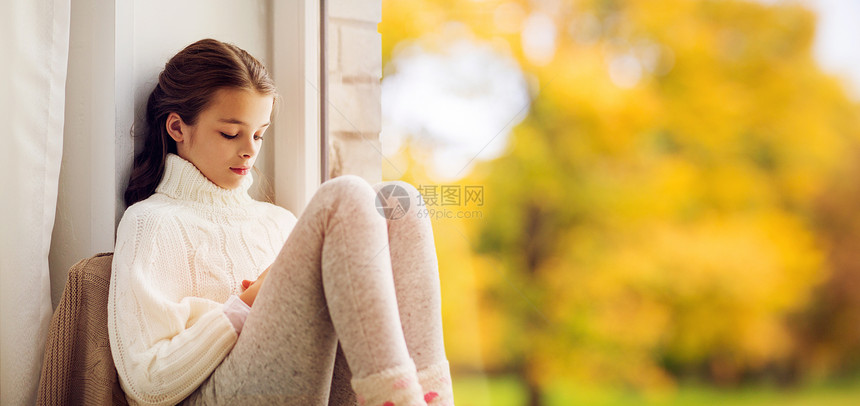 童,悲伤季节的悲伤的美丽女孩穿着毛衣坐家里的窗台上,秋天的背景下秋天,悲伤的女孩坐家里的窗台上图片