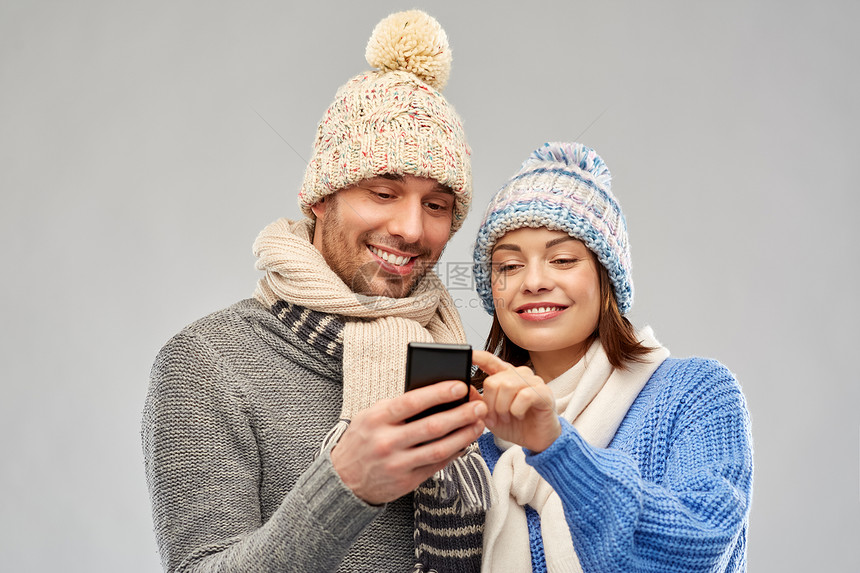 技术,诞节冬季服装幸福夫妇针帽围巾与智能手机灰色背景穿着冬天衣服智能手机的幸福夫妇图片