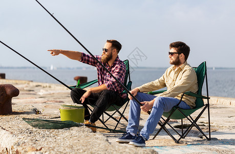 休闲人的男朋友与钓鱼竿坐营地椅子上的海上码头码头上钓竿的男朋友背景图片