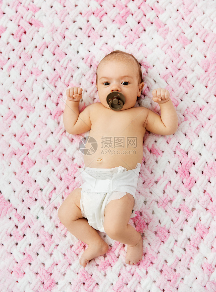 婴儿期人们的甜蜜的小女孩尿布上躺着,用奶嘴毛绒纱的针粉红色毯子上穿着尿布的女婴躺毯子上用奶嘴图片